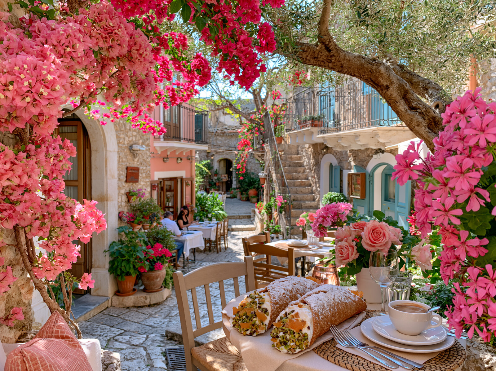 Cannoli and coffee on a café table in a sunny old street hung with pink bougainvillea
